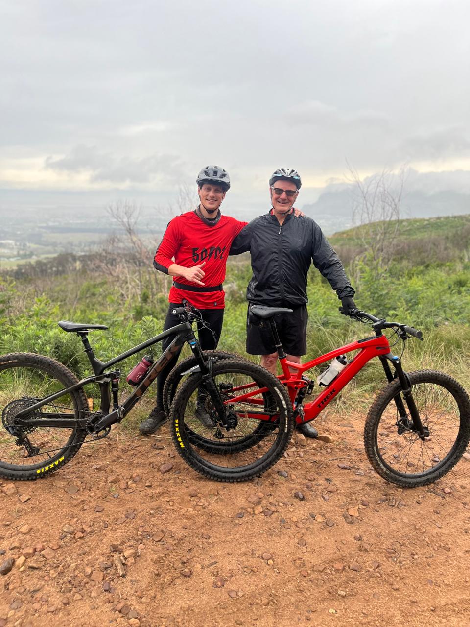 Two riders standing with their mountain bikes on a red gravel trail