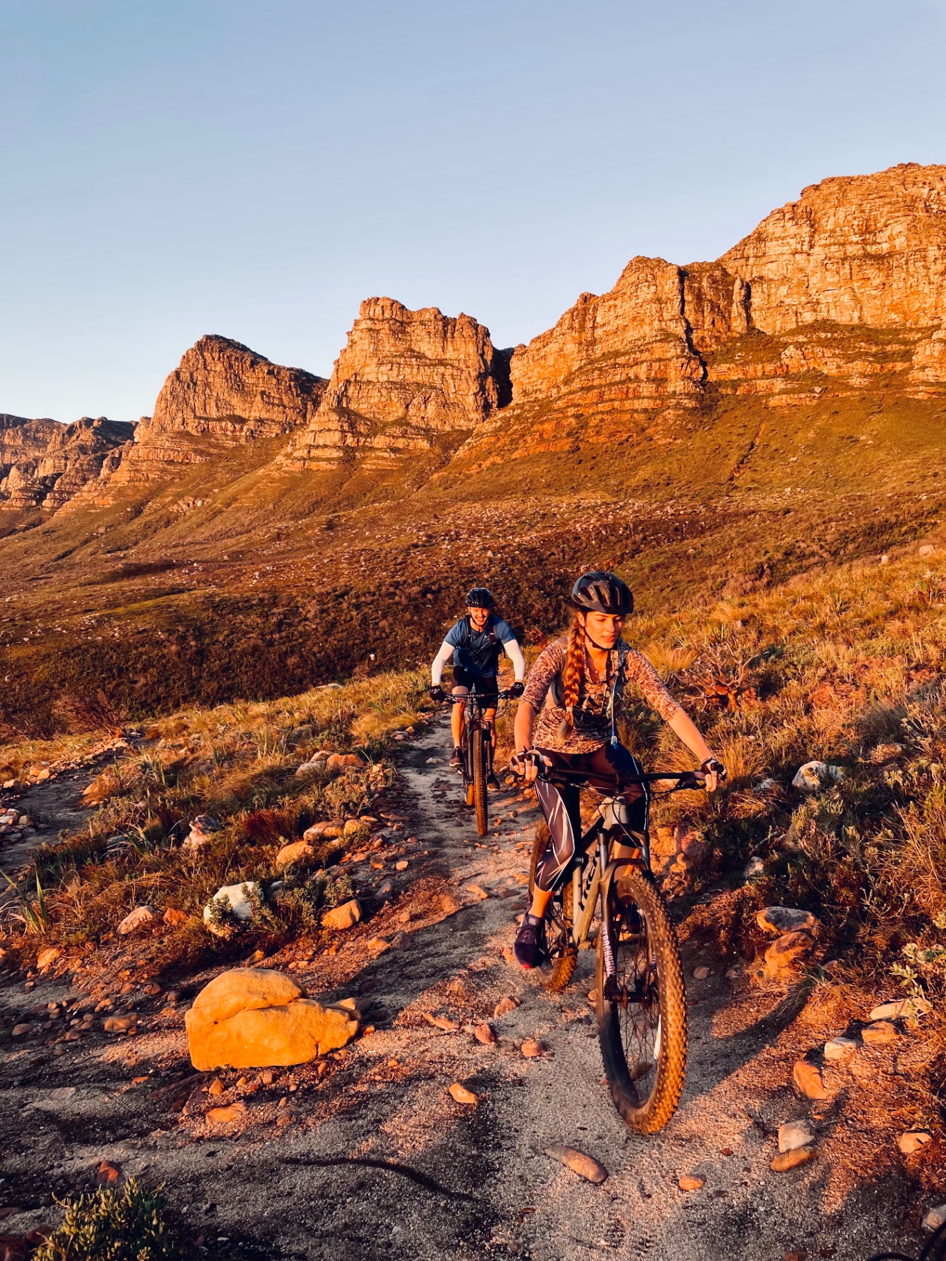 Two riders climb a rocky trail below the Twelve Apostles at sunset